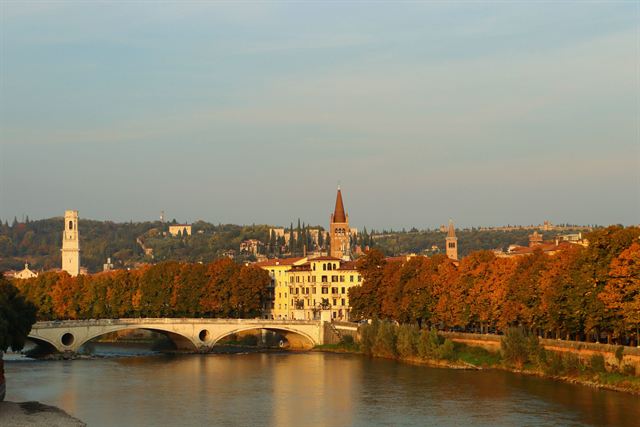 Ponte Pietra stone bridge over the Adige in Verona at golden hour with autumn trees and bell towers