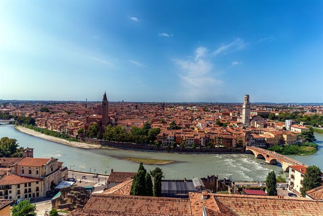 Panorama over Verona's terracotta rooftops, towers and the curving Adige River under blue sky