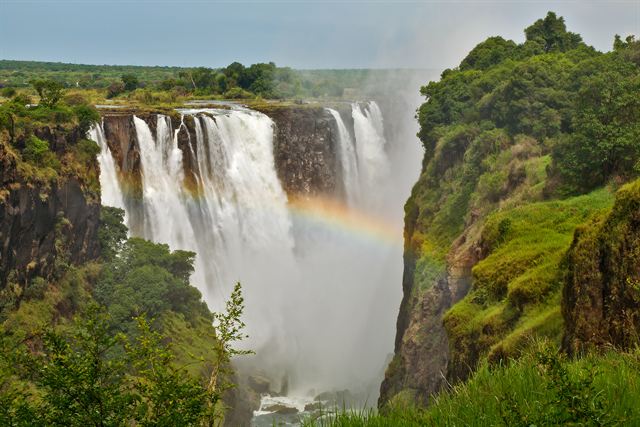 Victoria Falls cascading into a green gorge with a rainbow in the mist
