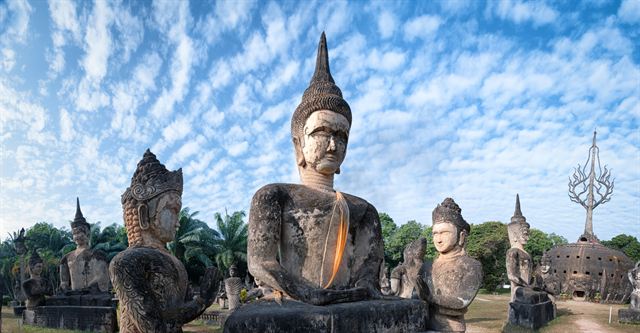 Large seated Buddha and deity statues in Vientiane's Buddha Park under a dappled sky