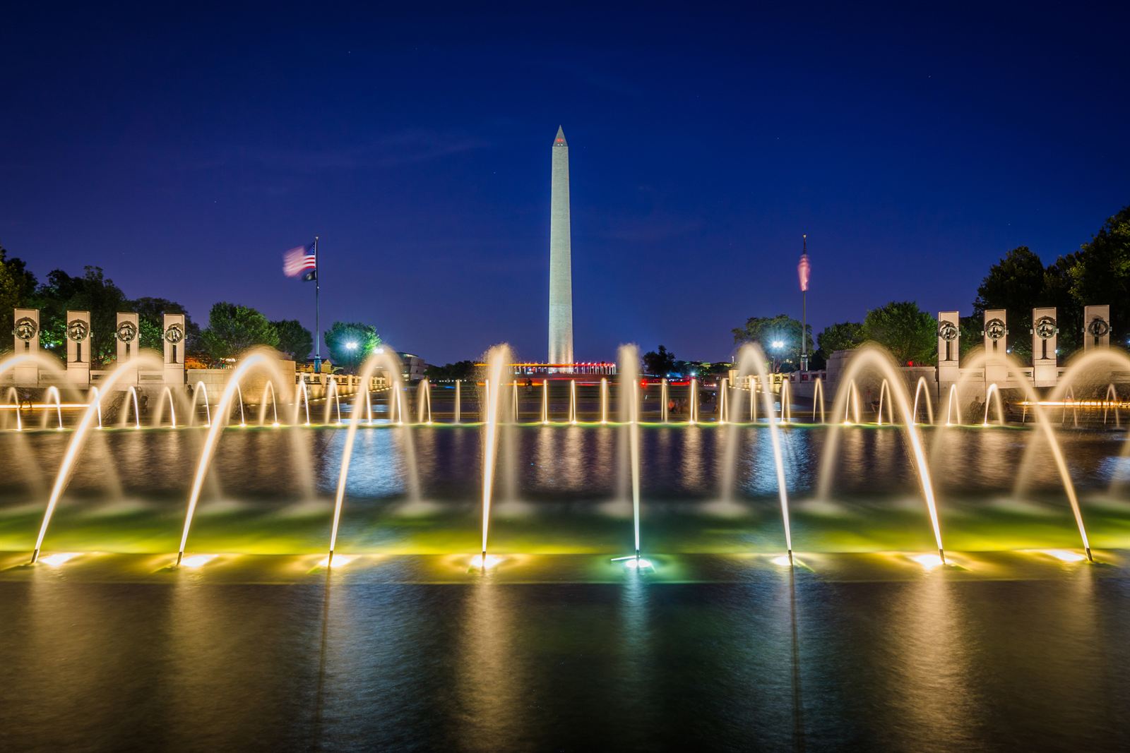 National World War II Memorial fountains lit at night with the Washington Monument