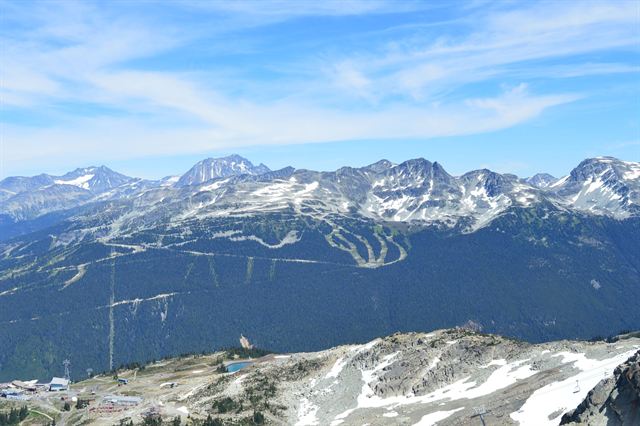 Snow-streaked Whistler and Blackcomb mountain ski runs above the forested valley in early summer