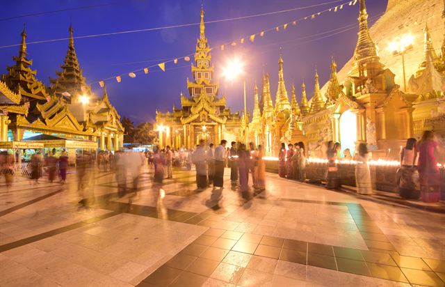 Golden stupas of Shwedagon Pagoda glowing at dusk with visitors on the marble terrace, Yangon