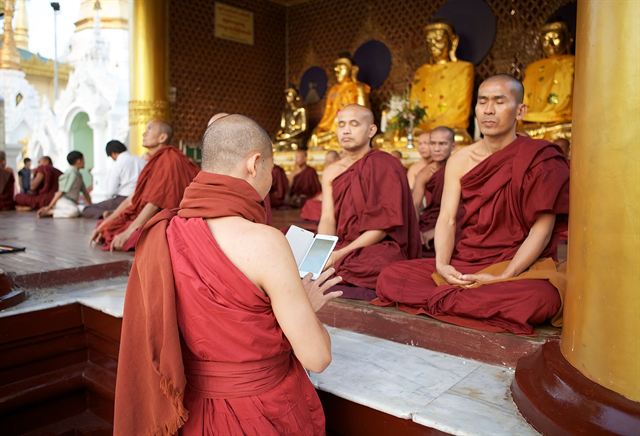 Buddhist monks in maroon robes seated before golden Buddha statues at Shwedagon Pagoda, Yangon