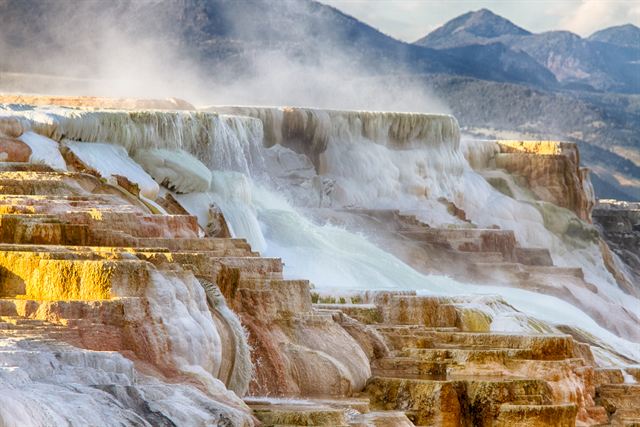 Travertine terraces of Mammoth Hot Springs steaming below mountains in Yellowstone