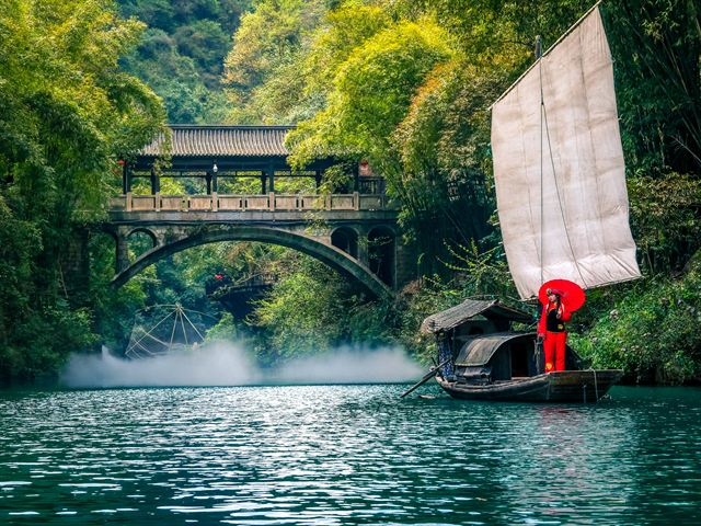 Sailing junk passing under a stone bridge at the Three Gorges Tribe scenic area, Yichang
