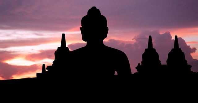 Silhouette of a Buddha and stupas at Borobudur against a pink sunrise sky