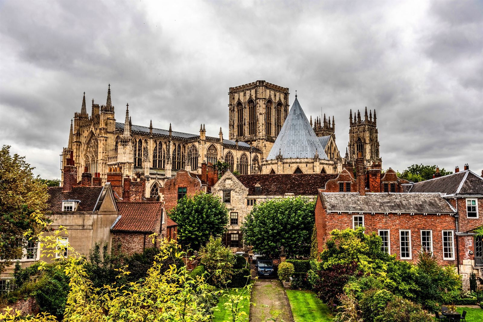York Minster's Gothic towers rising above green gardens and red-brick houses under cloudy sky