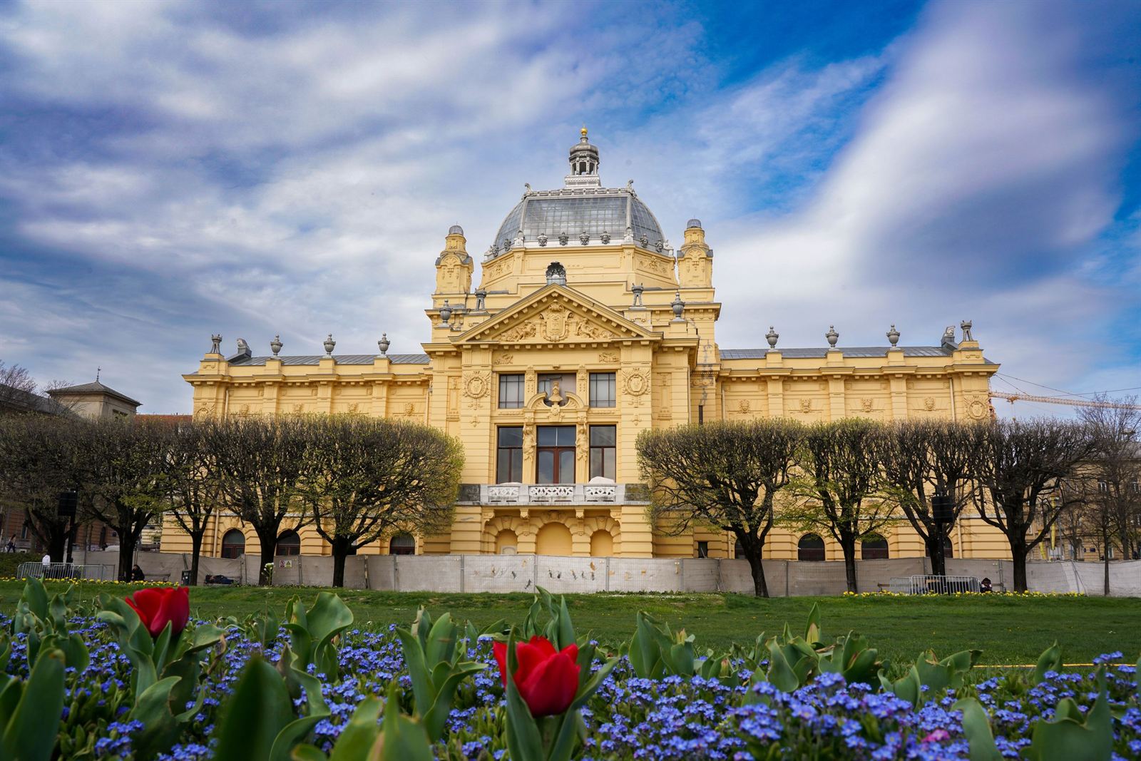 Yellow Art Pavilion (Umjetnički paviljon) in Zagreb behind spring tulips and forget-me-nots under dramatic sky