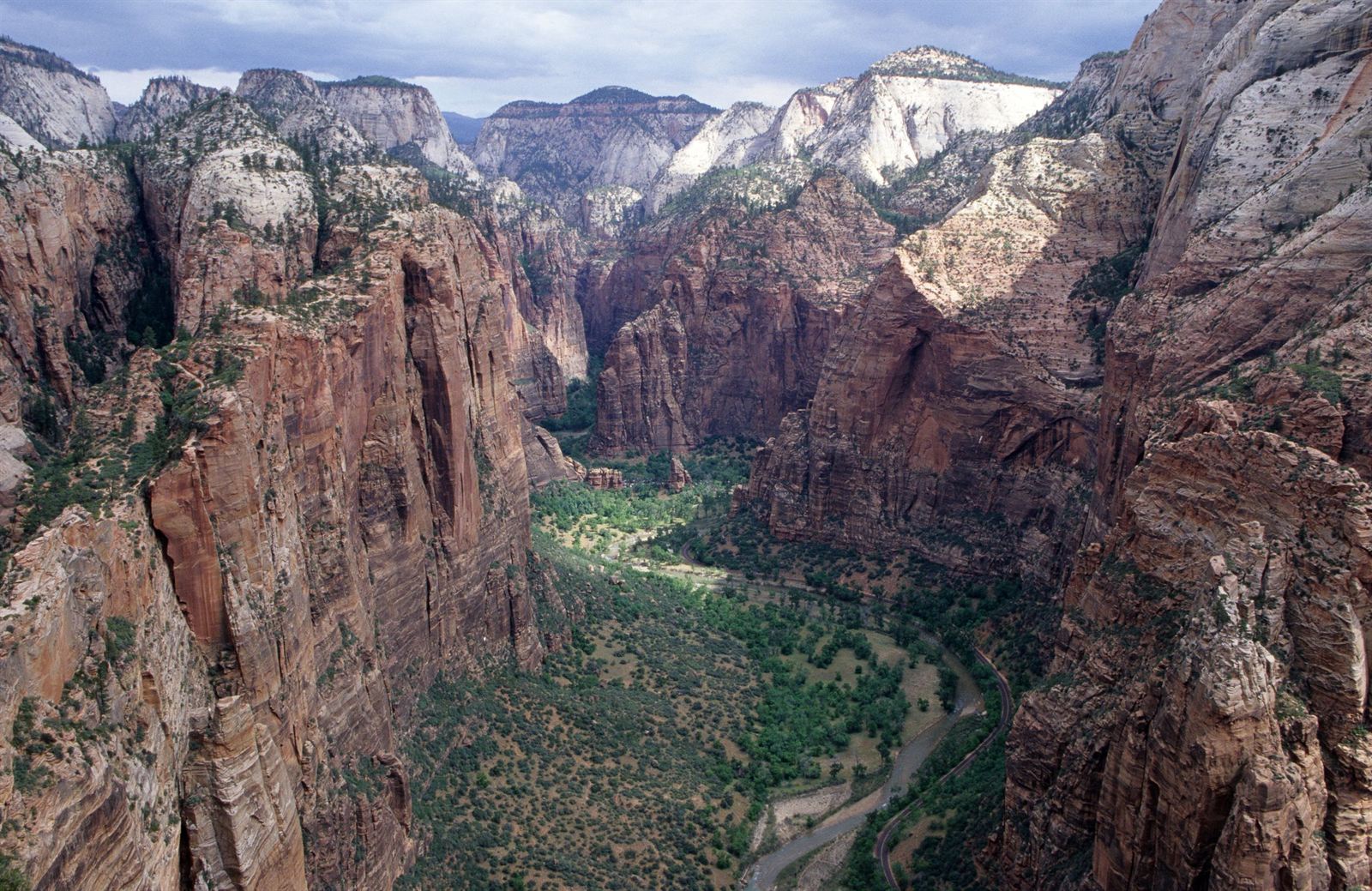 Towering sandstone walls of Zion Canyon with the Virgin River and road winding through the green valley floor